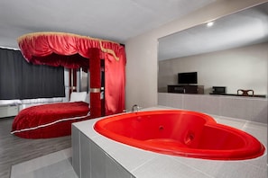 Ein modernes Hotelzimmer mit einem roten Himmelbett, einer großen, roten Badewanne und einem Fernseher an der Wand.