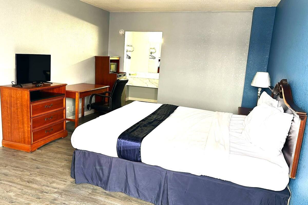 Une chambre d’hôtel comprenant un lit, une commode en bois, un bureau, une télévision et un miroir.