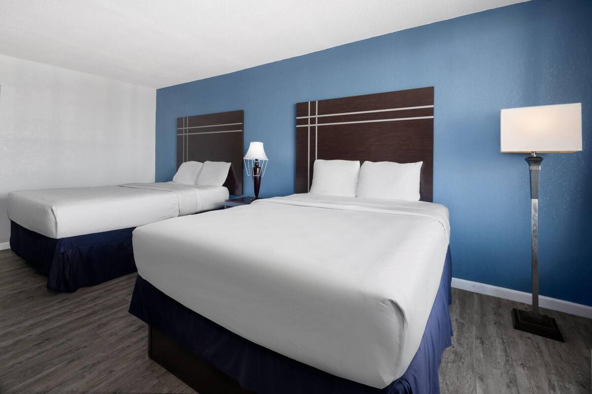 Une chambre d’hôtel avec deux lits, une table de chevet avec une lampe et un mur d’accent bleu.