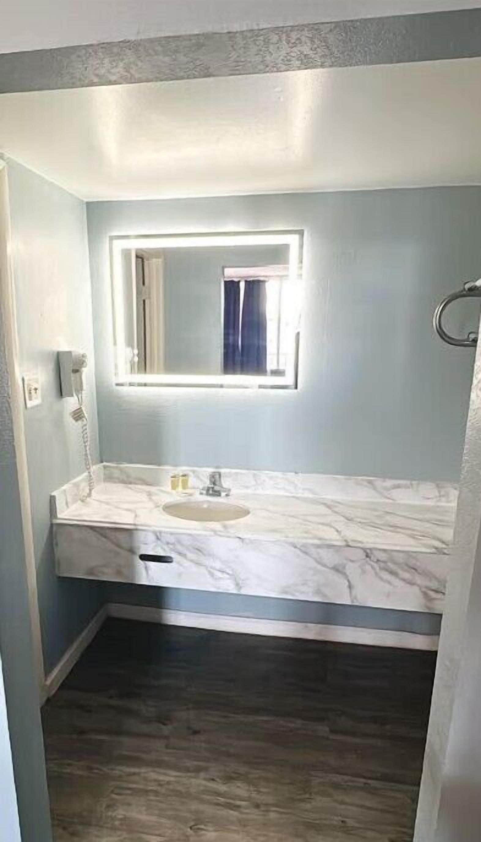 A bathroom with a marble countertop, a sink, a mirror, and a shower area.