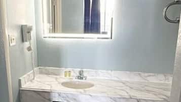Um banheiro com bancada de mármore, pia, espelho e chuveiro.