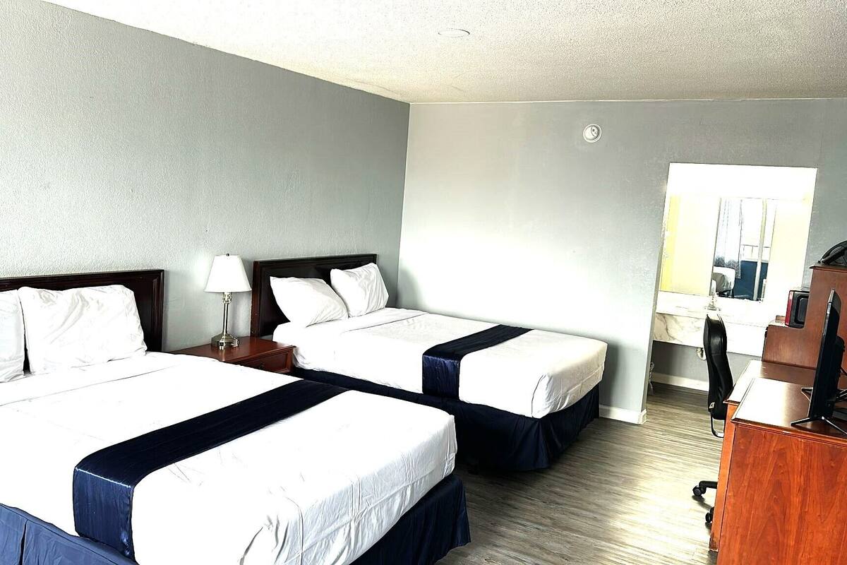 Une chambre d’hôtel avec deux lits, un bureau, une chaise, une lampe et un miroir.