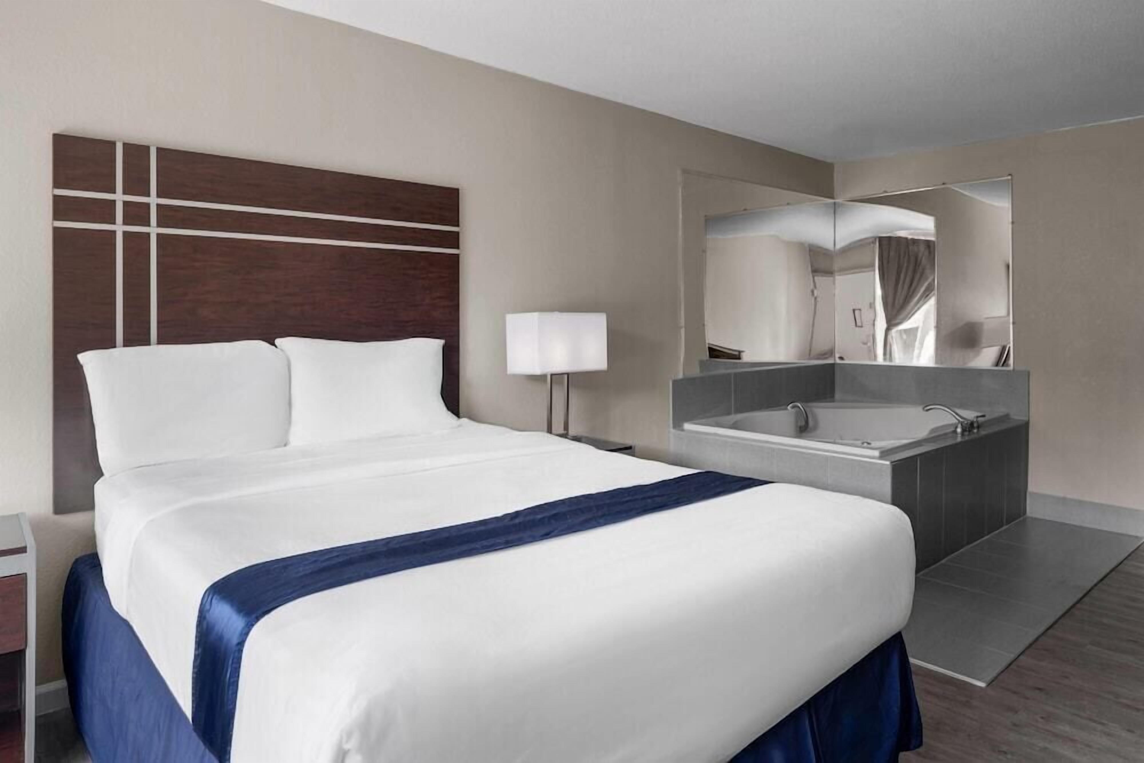 Ein Hotelzimmer mit einem großen Bett, einem Badezimmer mit einer Badewanne und einem Spiegel.