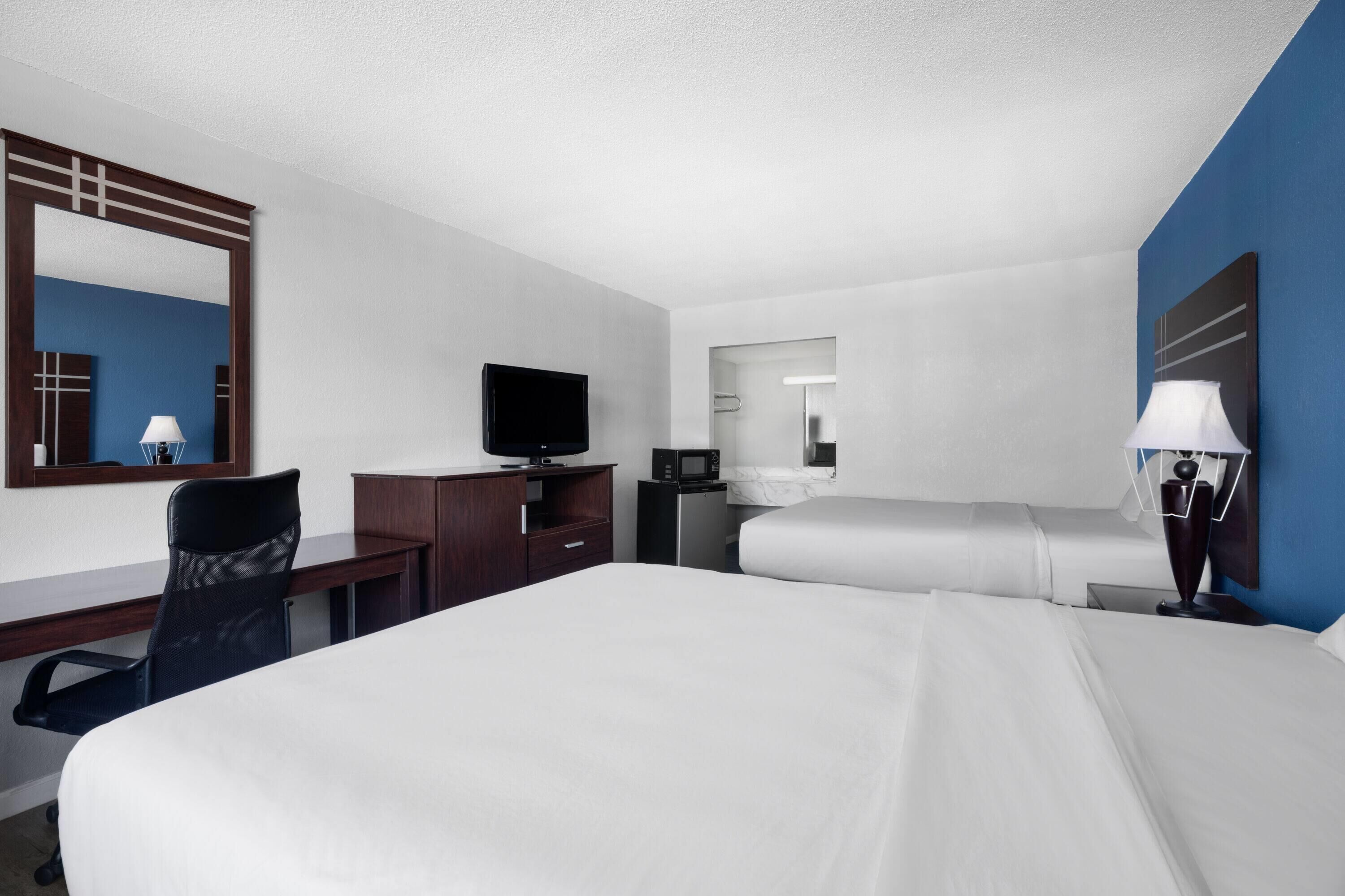 A hotel room with a large bed, a desk with a chair, a television, a microwave, and a bathroom visible through an open door.