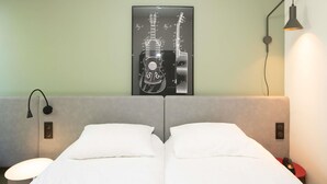 A hotel room with a bed, two pillows, a wall-mounted lamp, and a framed guitar artwork. - ibis Reims Tinqueux (Tinqueux)
