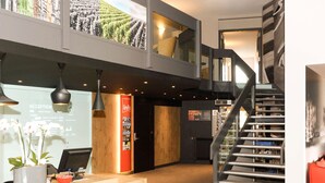 A modern hotel lobby with a reception desk, a staircase, and a view of a vineyard. - ibis Reims Tinqueux (Tinqueux)