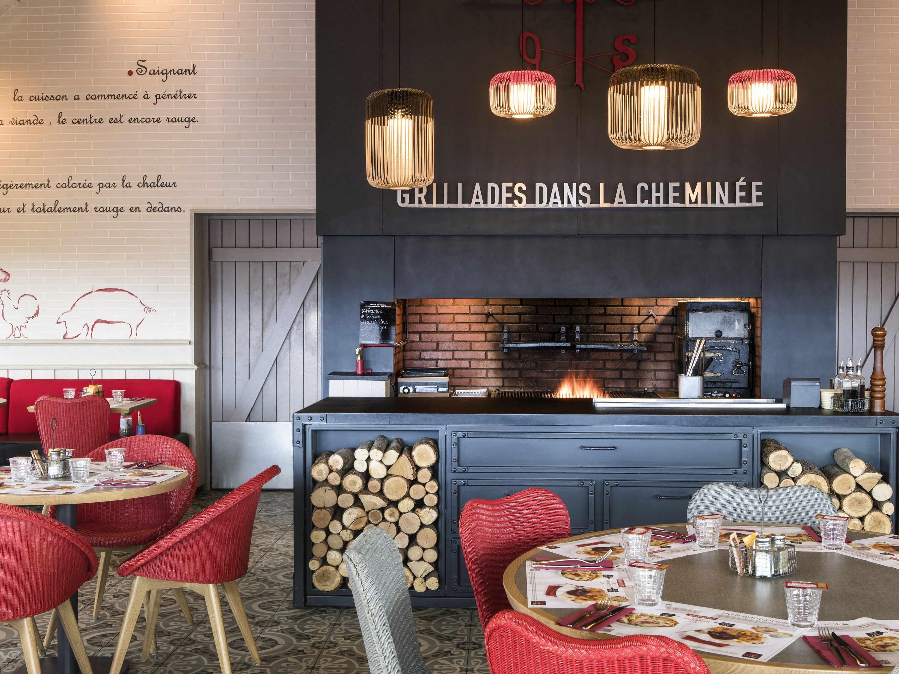 L’intérieur d’un restaurant avec des sièges rembourrés de couleur rouge, une cheminée en briques et des lampes suspendues.