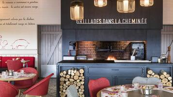 L’intérieur d’un restaurant avec des sièges rembourrés de couleur rouge, une cheminée en briques et des lampes suspendues.