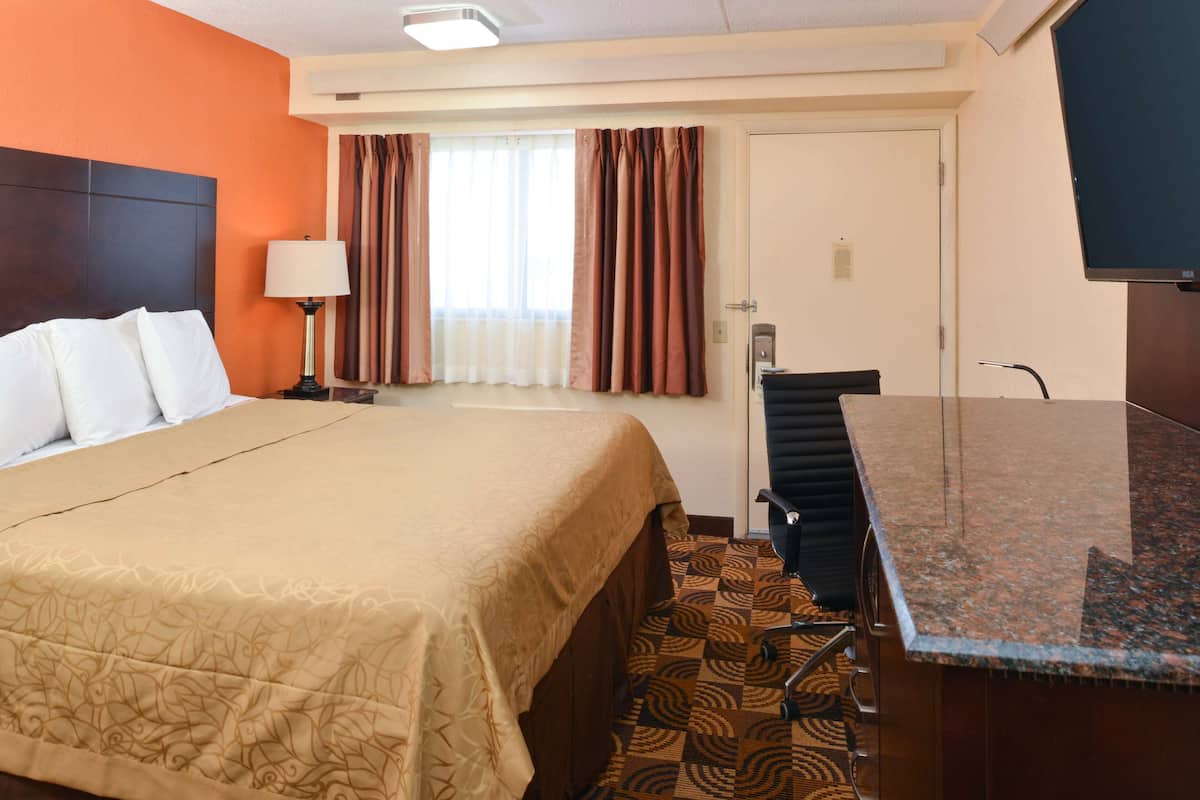 Een hotelkamer met een bed, een bureau, een stoel, een lamp en een raam met gordijnen.