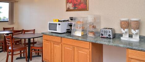 Eine kleine Küchenzeile mit einer Mikrowelle, einem Toaster und Kaffeeautomaten auf der Arbeitsfläche, ein Esstisch mit Stühlen und ein Bild an der Wand.