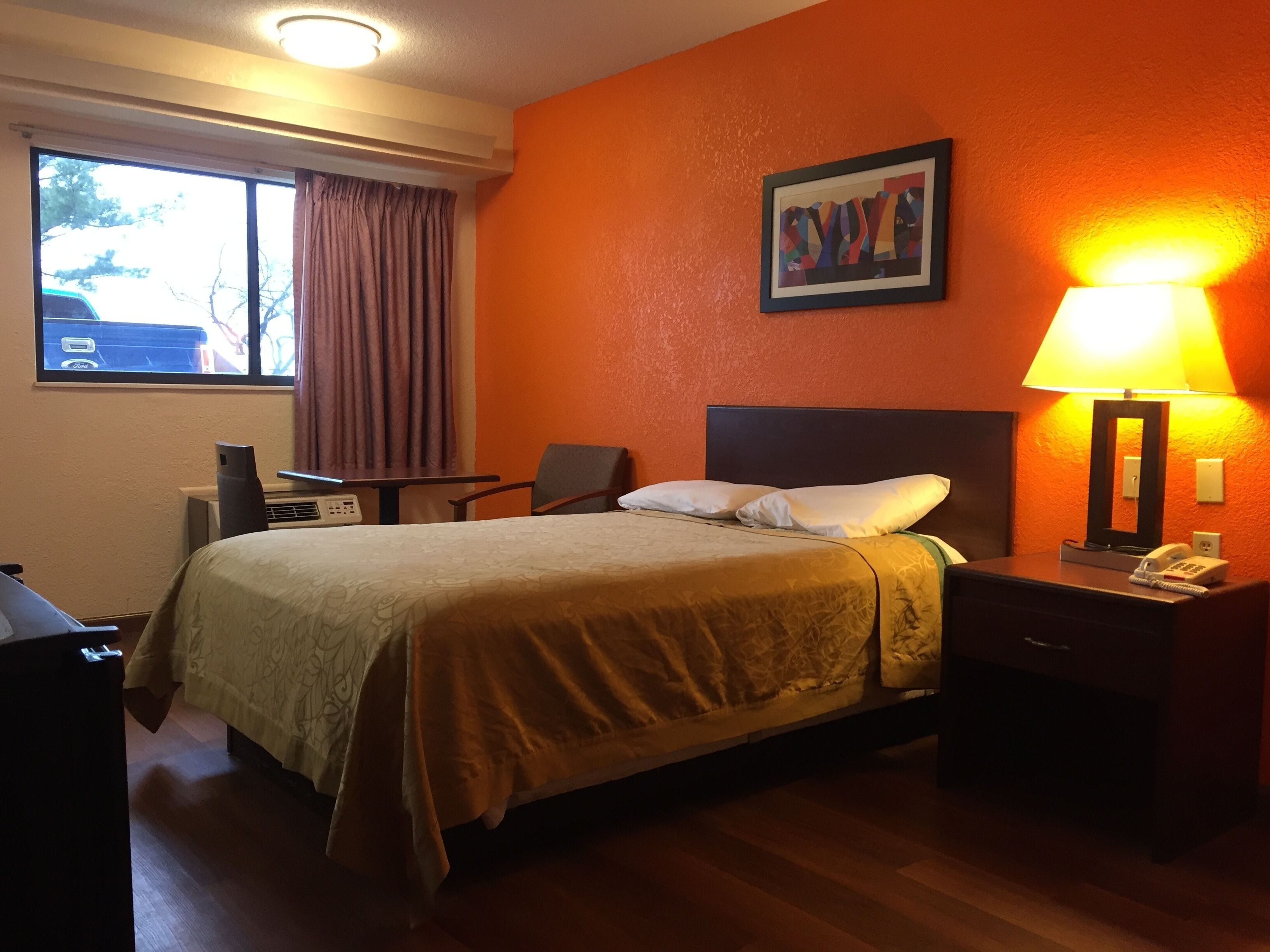 A hotel room with a bed, a desk, a chair, a lamp, and a painting on the wall.