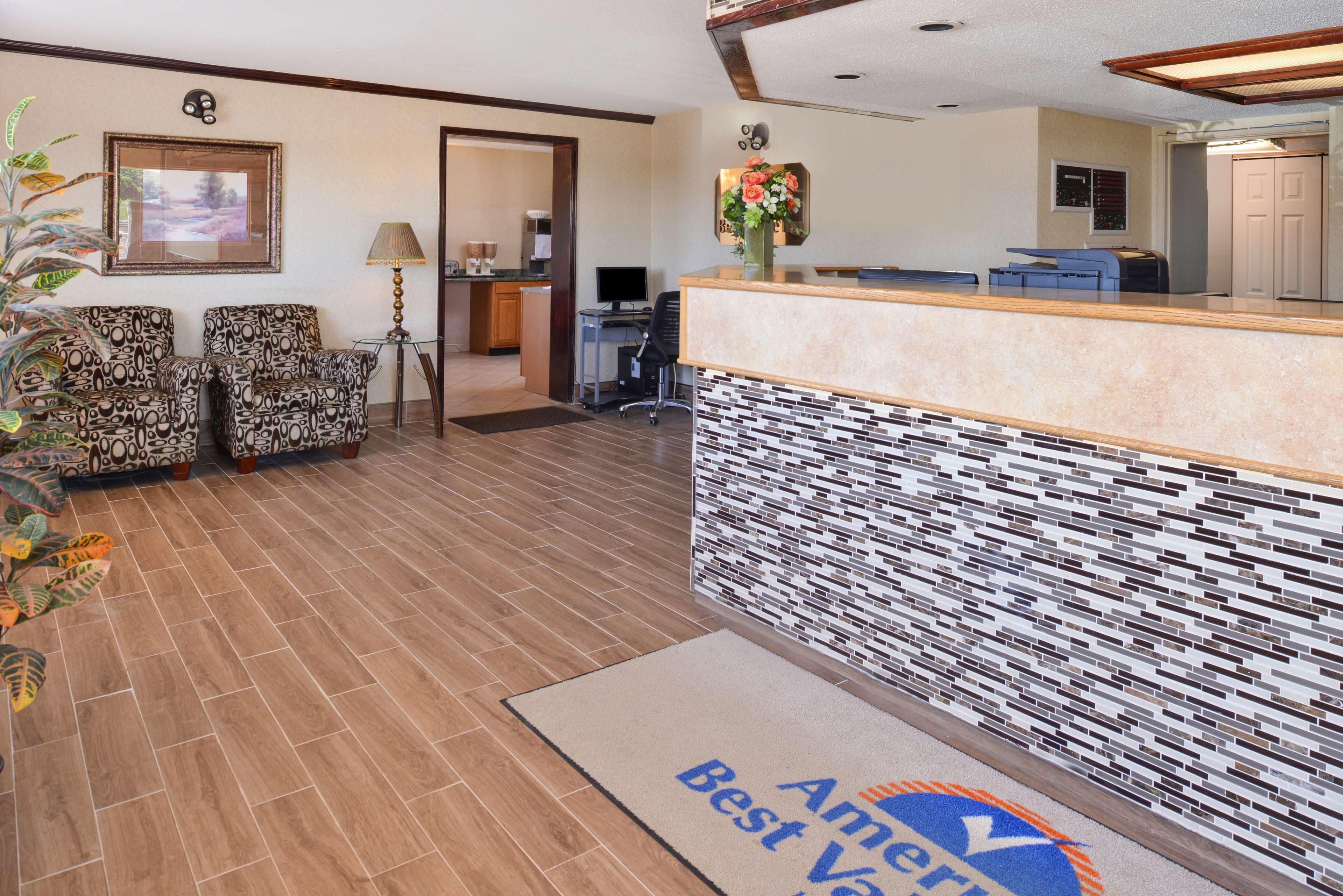 A reception area with patterned chairs, a reception desk, a computer, and a door leading to a kitchen area.