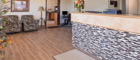 Un área de recepción con sillas estampadas, un mostrador de recepción, una computadora y una puerta que da a una zona de cocina.