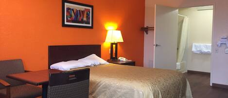 A hotel room with a bed, a desk, a chair, a lamp, and a bathroom visible through an open door.