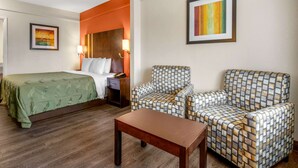 Une chambre d’hôtel avec un lit, deux fauteuils à motifs, une petite table et un tableau au mur.