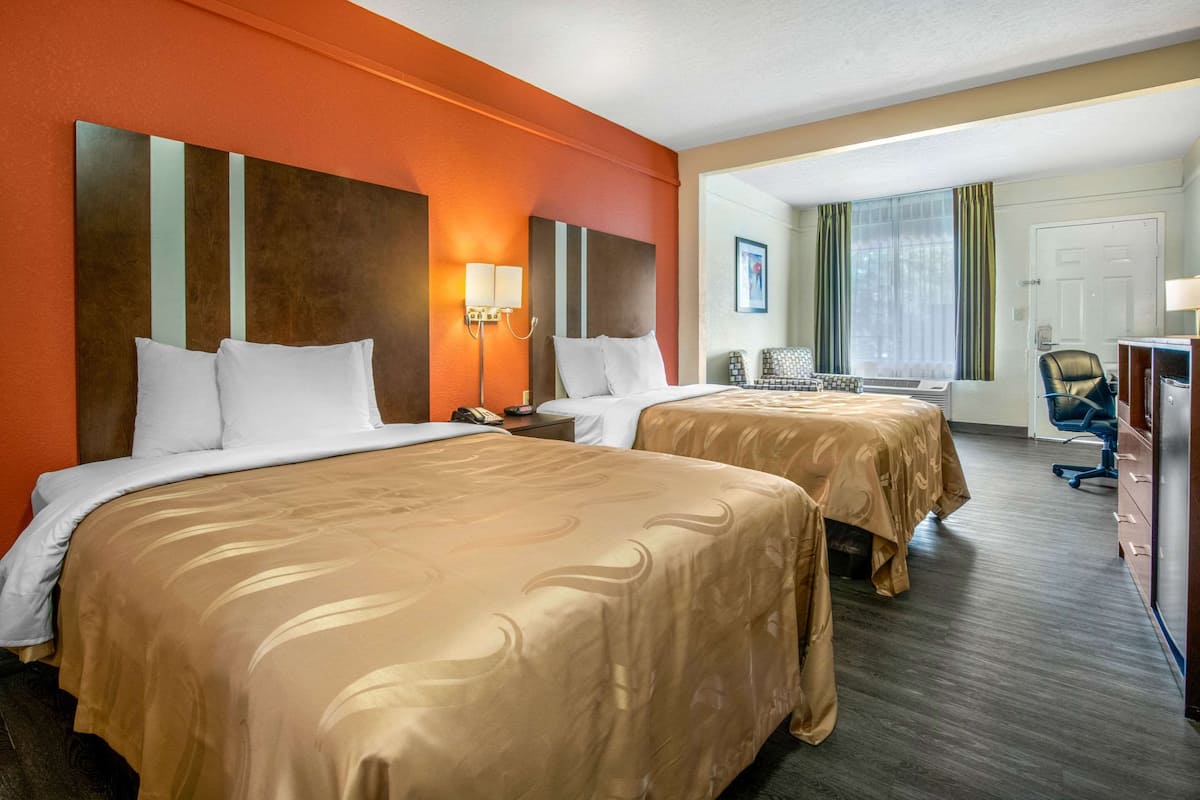 Une chambre d’hôtel avec deux lits, un bureau, une chaise et une fenêtre avec des rideaux.