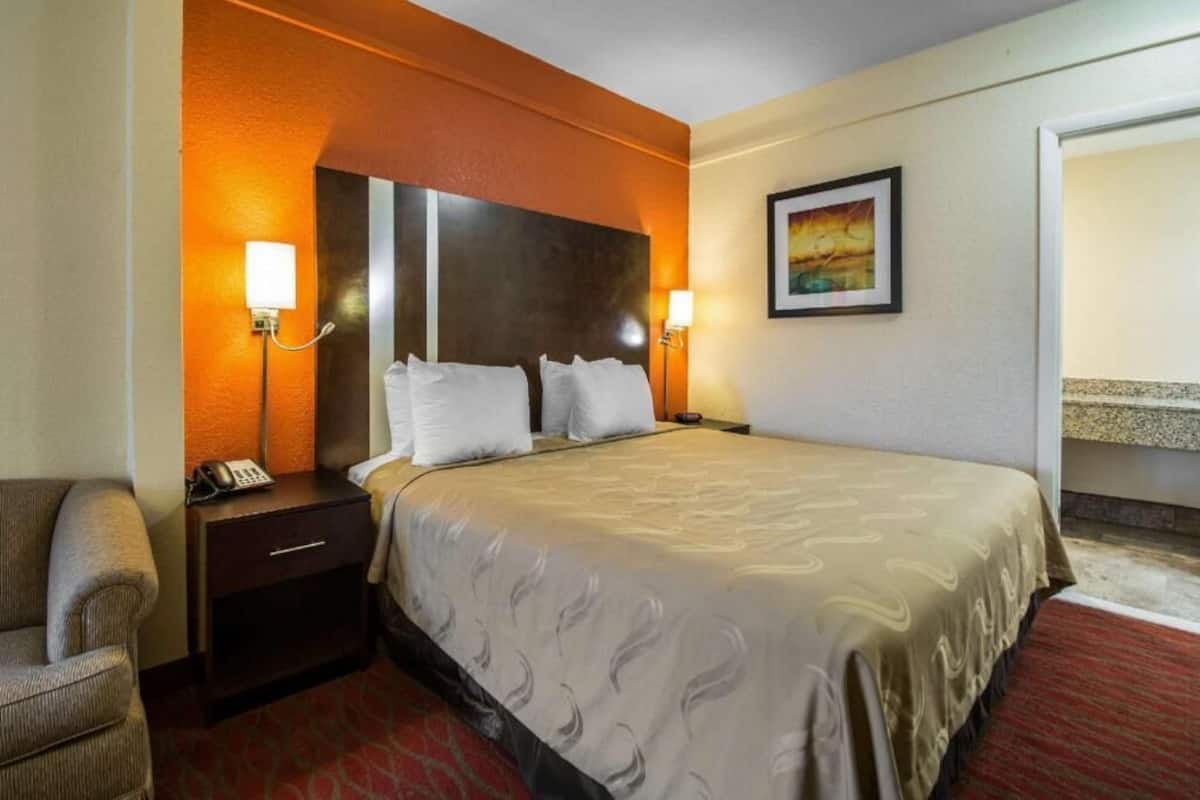 Une chambre d’hôtel avec un grand lit, deux lampes de chevet, une table de chevet avec un téléphone, une chaise et un tableau au mur.