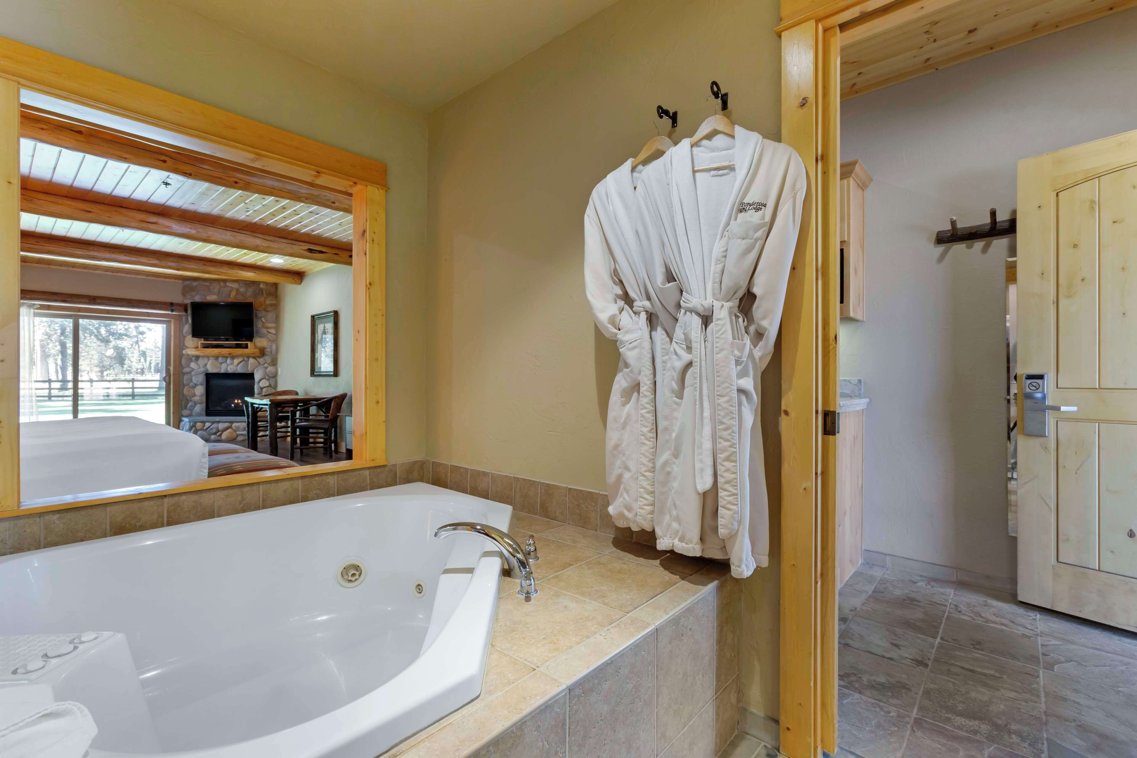 A bathroom with a large bathtub, a wooden ceiling, and a stone fireplace.