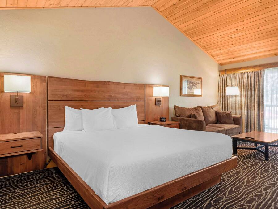 Una cama grande con cabecera de madera, mesitas de noche, un sofá y una pequeña mesa.