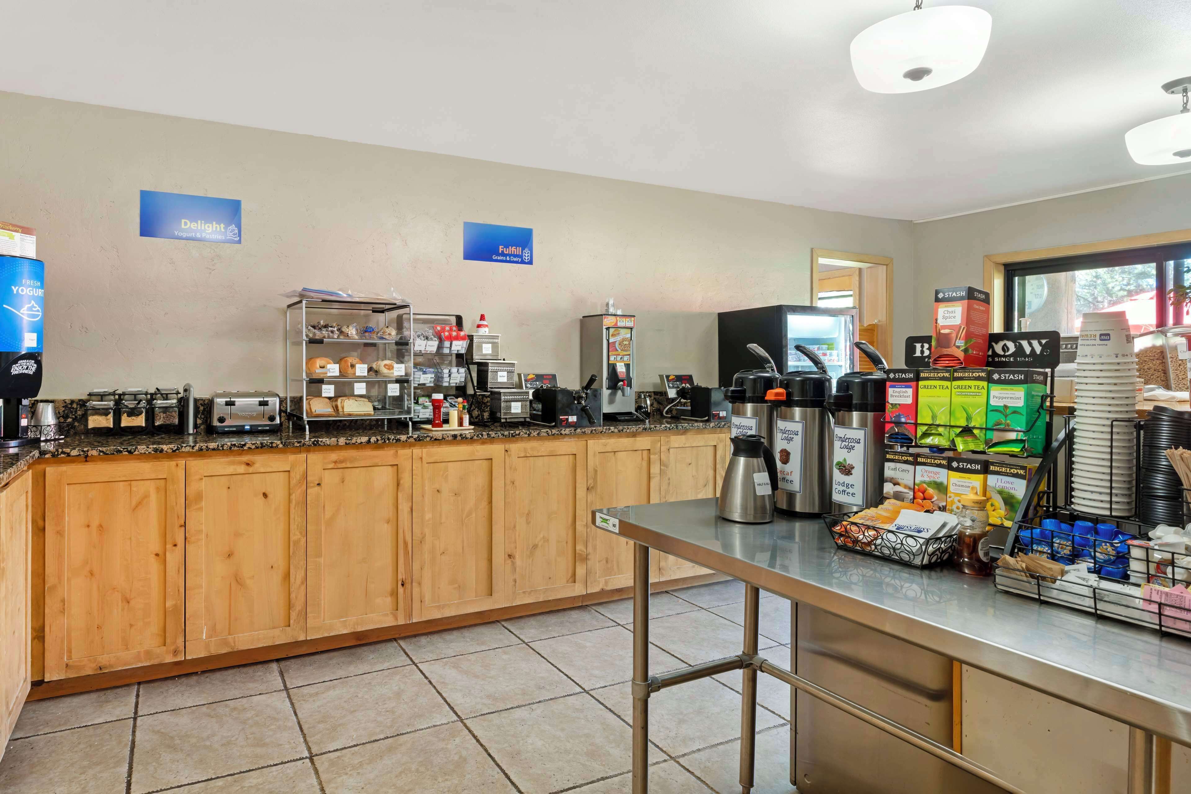 Un área de desayuno autoservicio con diversas opciones de comida y bebida, que incluye cafeteras, un refrigerador y una selección de aperitivos y bebidas.