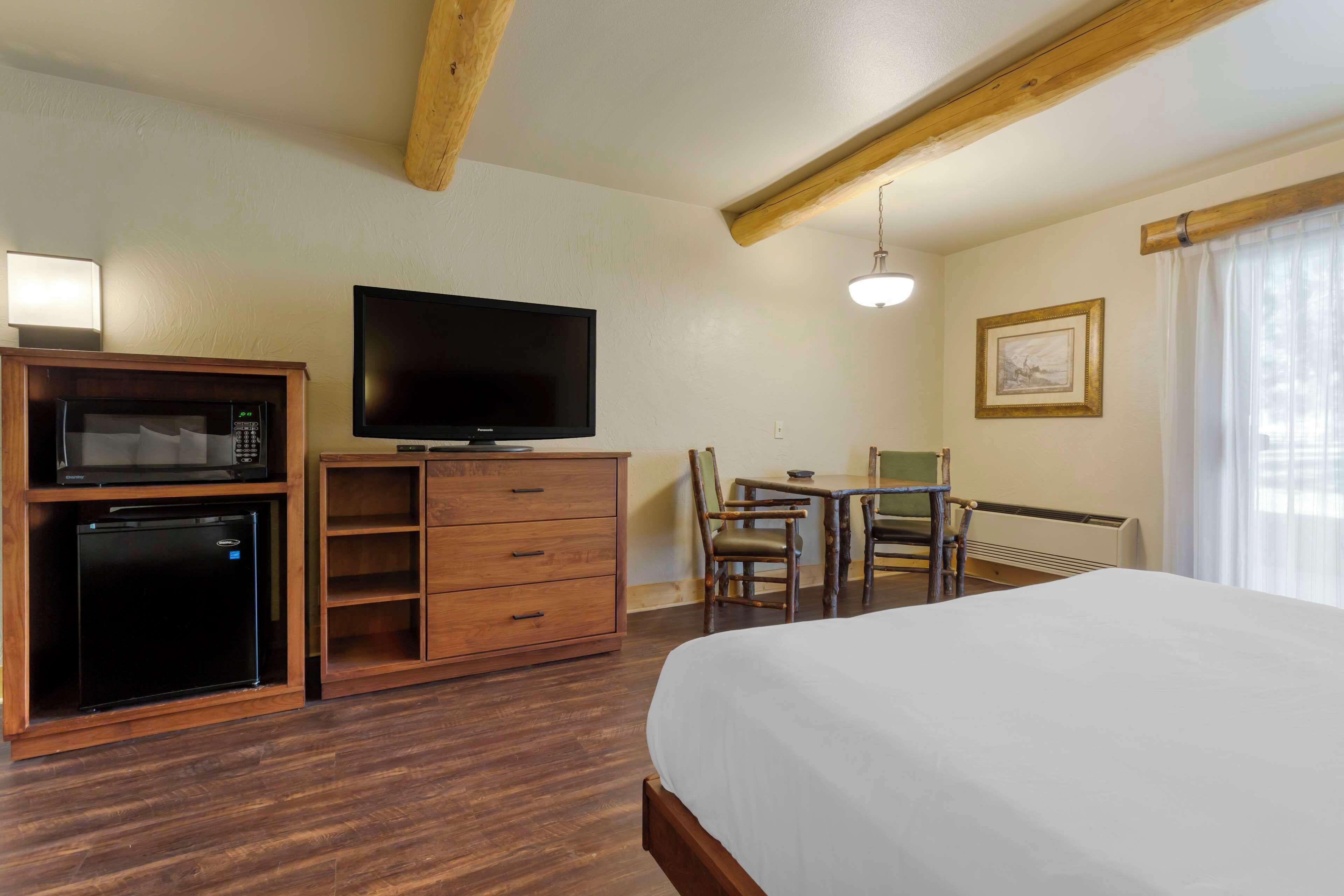 A hotel room with a bed, a desk with a chair, a television, a microwave, and a refrigerator.