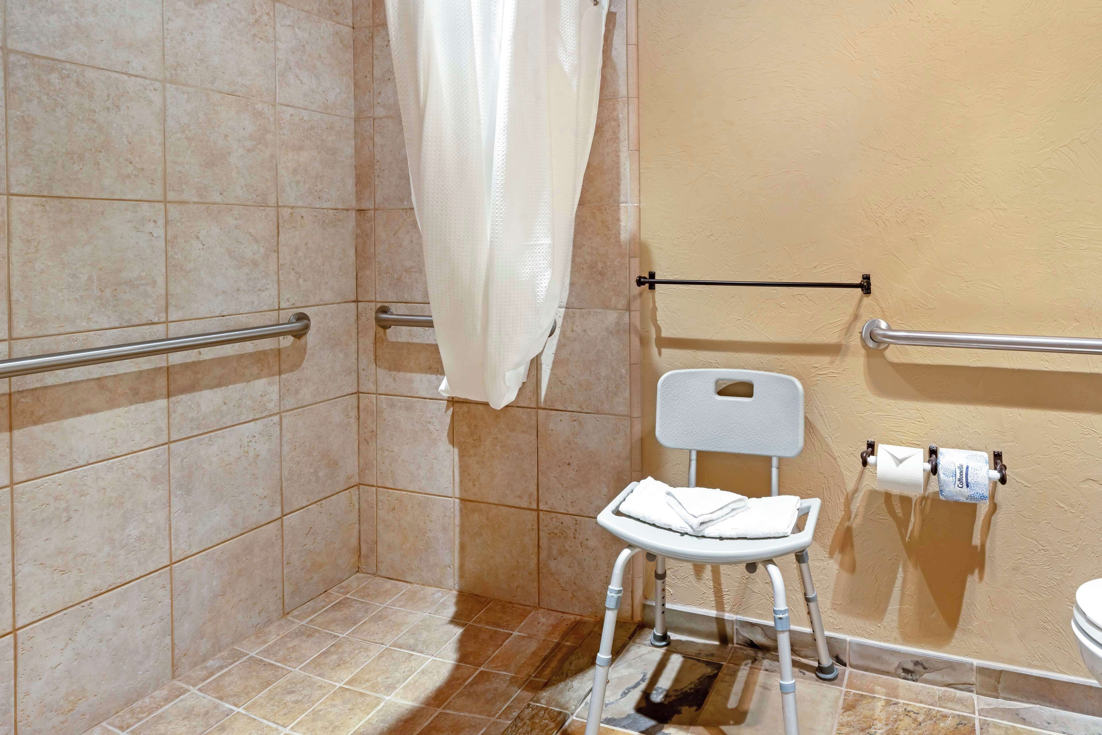 A bathroom with a shower area, a toilet, and a chair.