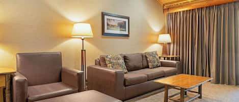 A cozy room with a brown leather sofa, a matching armchair, and a wooden coffee table. There are two floor lamps and a framed picture on the wall.