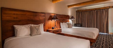 A hotel room with two beds, wooden headboards, a nightstand with lamps, and a checkered curtain.
