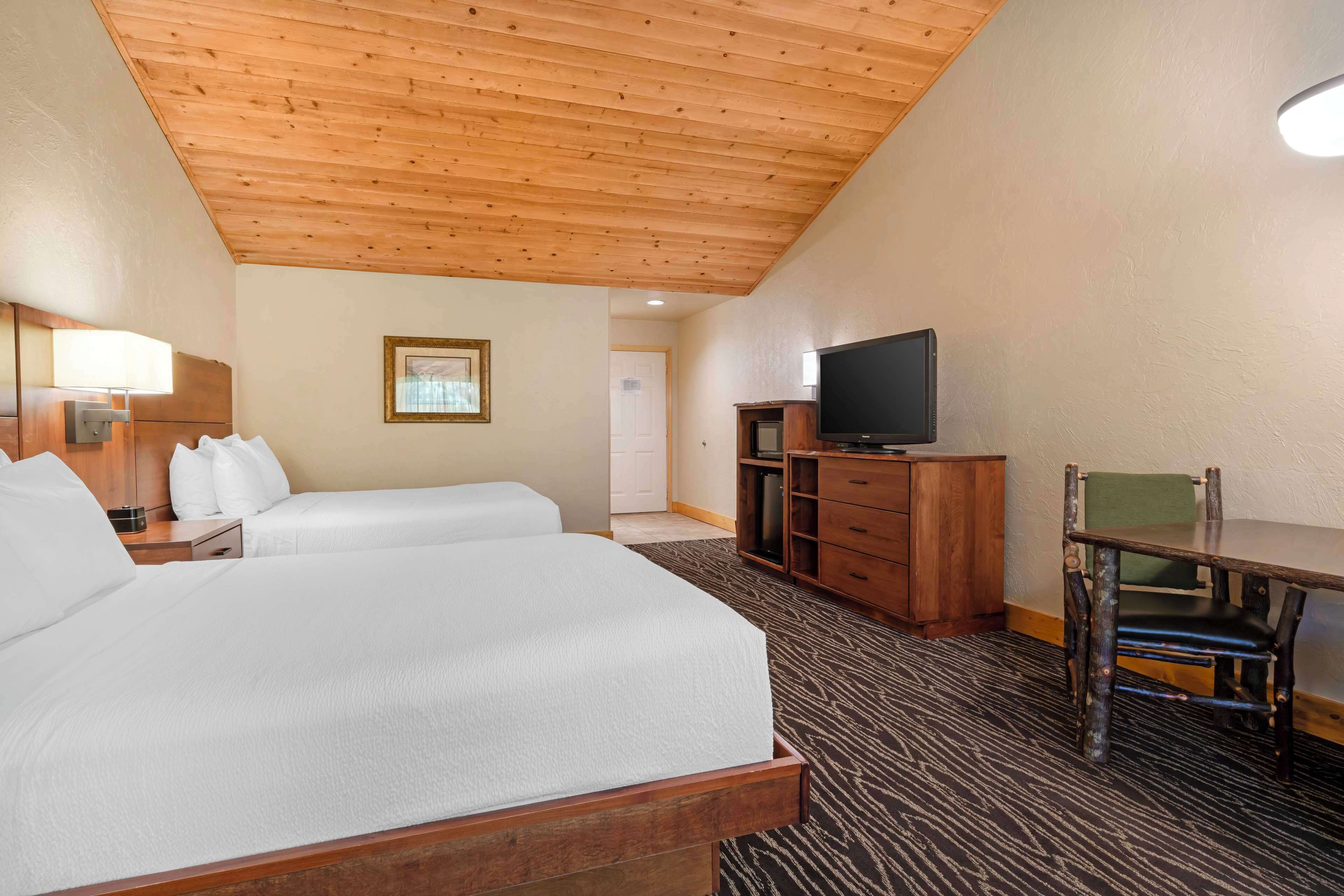 A hotel room with two beds, a wooden ceiling, a television, a desk, and a chair.