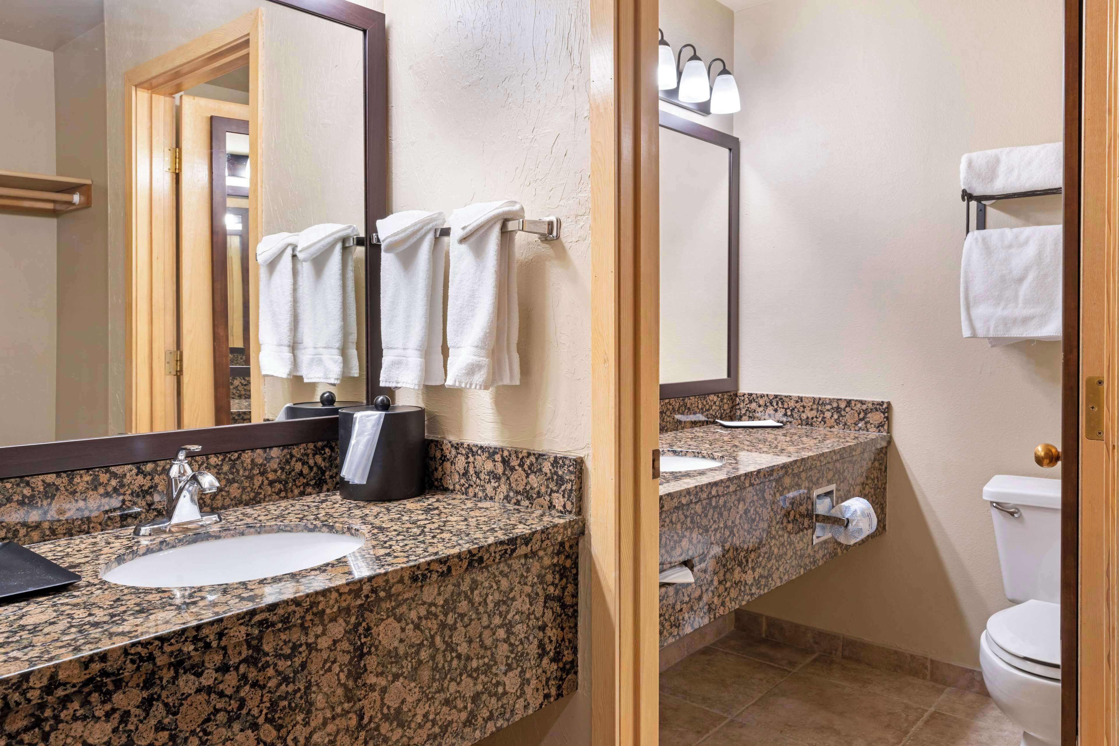 A bathroom with a granite countertop sink, a mirror, and a toilet.