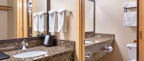 A bathroom with a granite countertop sink, a mirror, and a toilet.