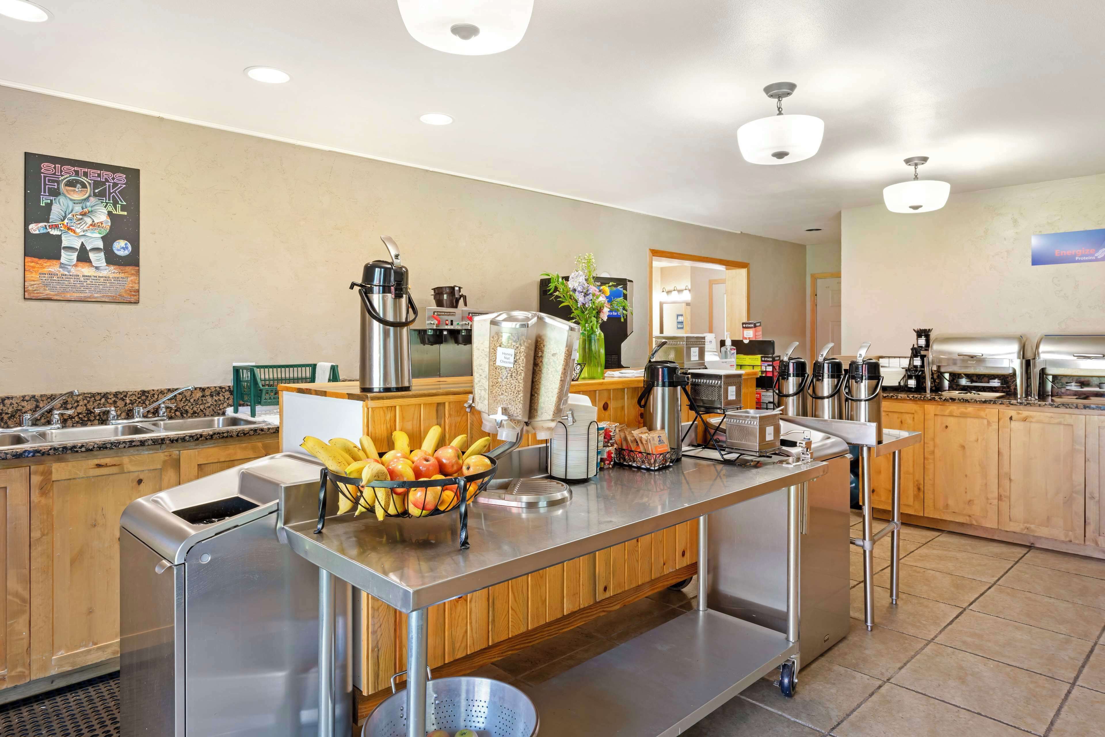 Zona de desayuno autoservicio con fruteros, máquinas de café y una barra de buffet.