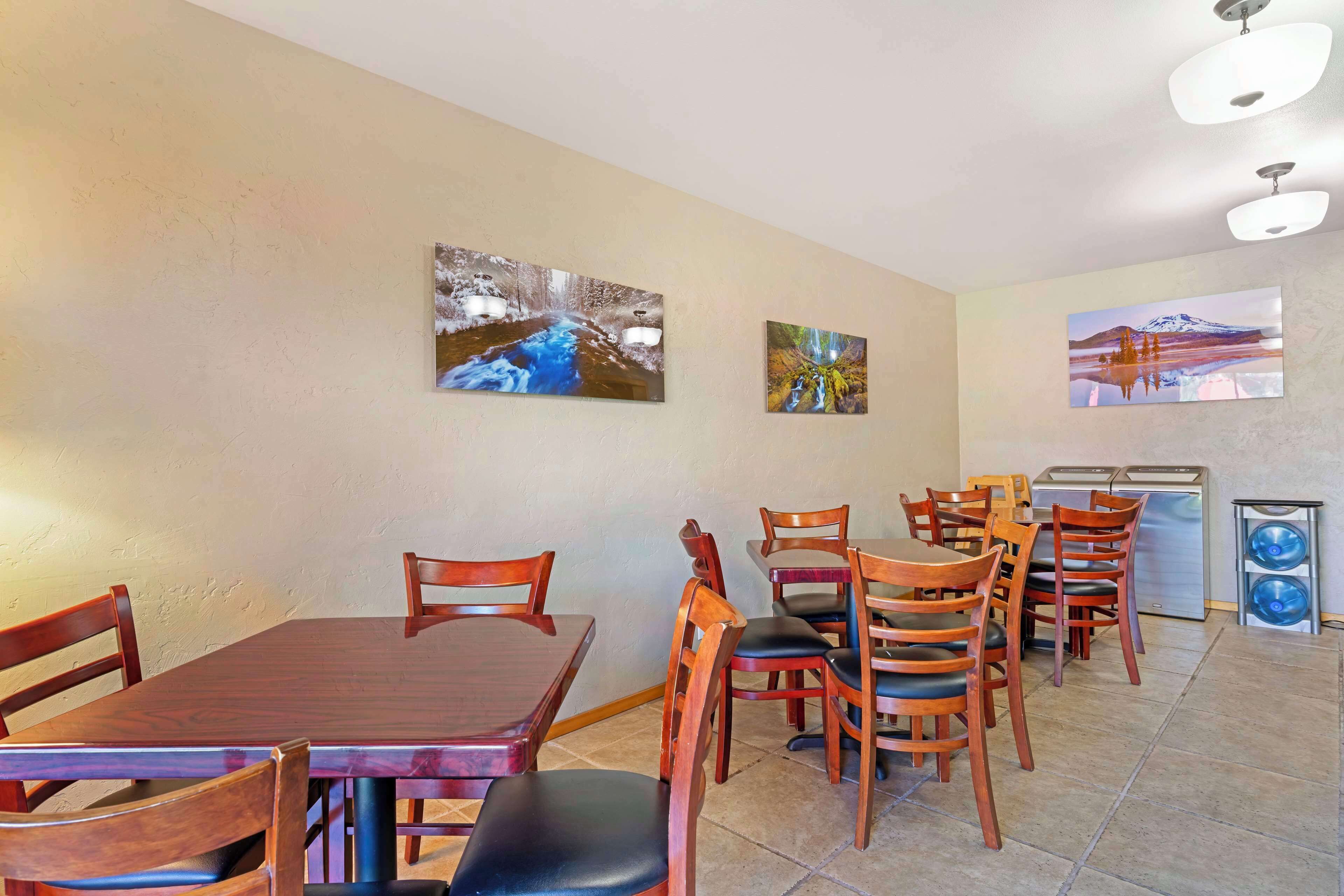 A dining area with wooden tables and chairs, a refrigerator, and two wall-mounted paintings.