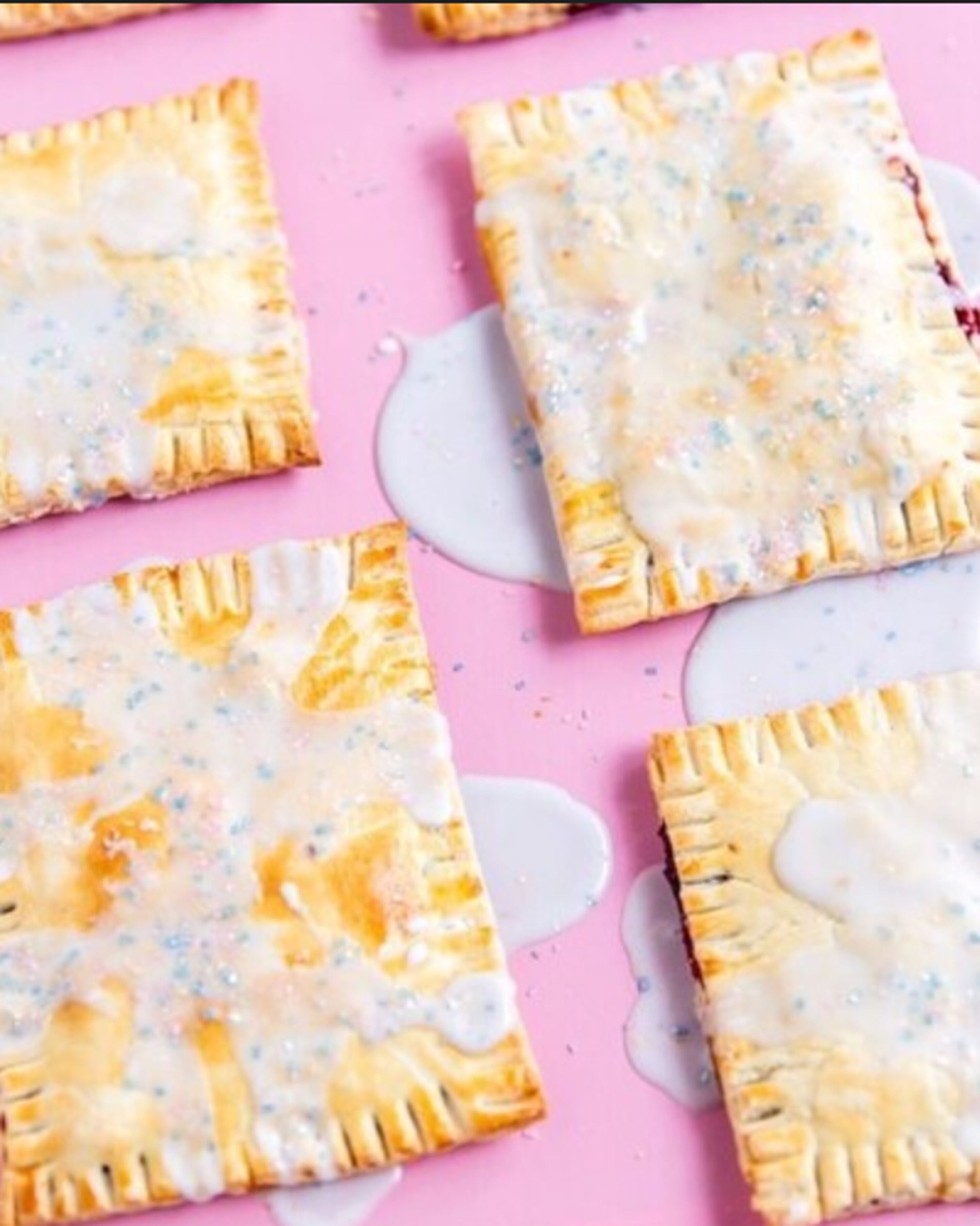 Four square pastries with a golden-brown crust and a white, speckled topping, arranged on a pink surface.