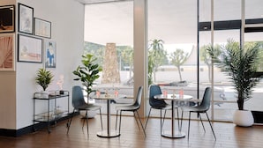 Un espacio interior moderno con zona de comedor que incluye mesas y sillas redondas, una planta en maceta y un pilar de piedra.