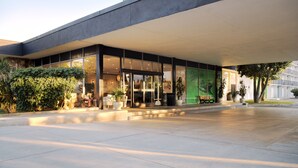 Un edificio moderno con una amplia entrada de vidrio, asientos exteriores y plantas en macetas.