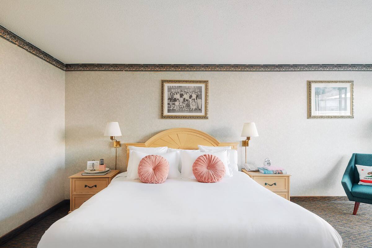 Habitación de hotel con una cama grande, dos mesitas de noche, un pequeño escritorio, una silla y dos cuadros en la pared.