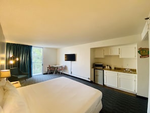 Ein Hotelzimmer mit einem großen Bett, einem kleinen Esstisch mit Stühlen, einem an der Wand montierten Fernseher, einer Küchenzeile mit Schränken und einem Schild an der Wand mit der Aufschrift 'EAT HERE'.