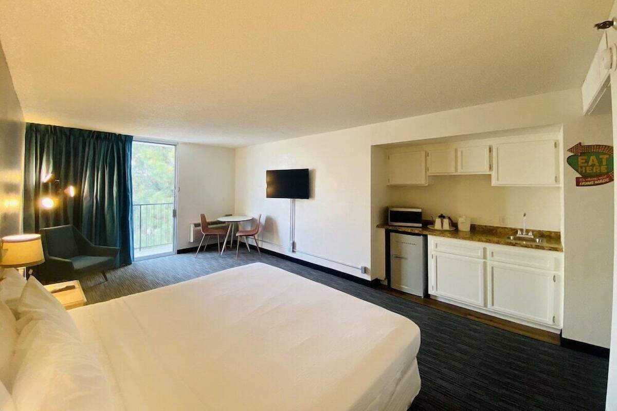Habitación de hotel con cama, escritorio y silla, televisor, kitchenette y balcón.