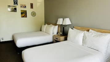 Une chambre d’hôtel avec deux lits, une table de chevet avec une lampe et des éléments de décoration murale, notamment un panneau indiquant la « Pacific Coast Highway » et une planche de surf « Hang Ten ».