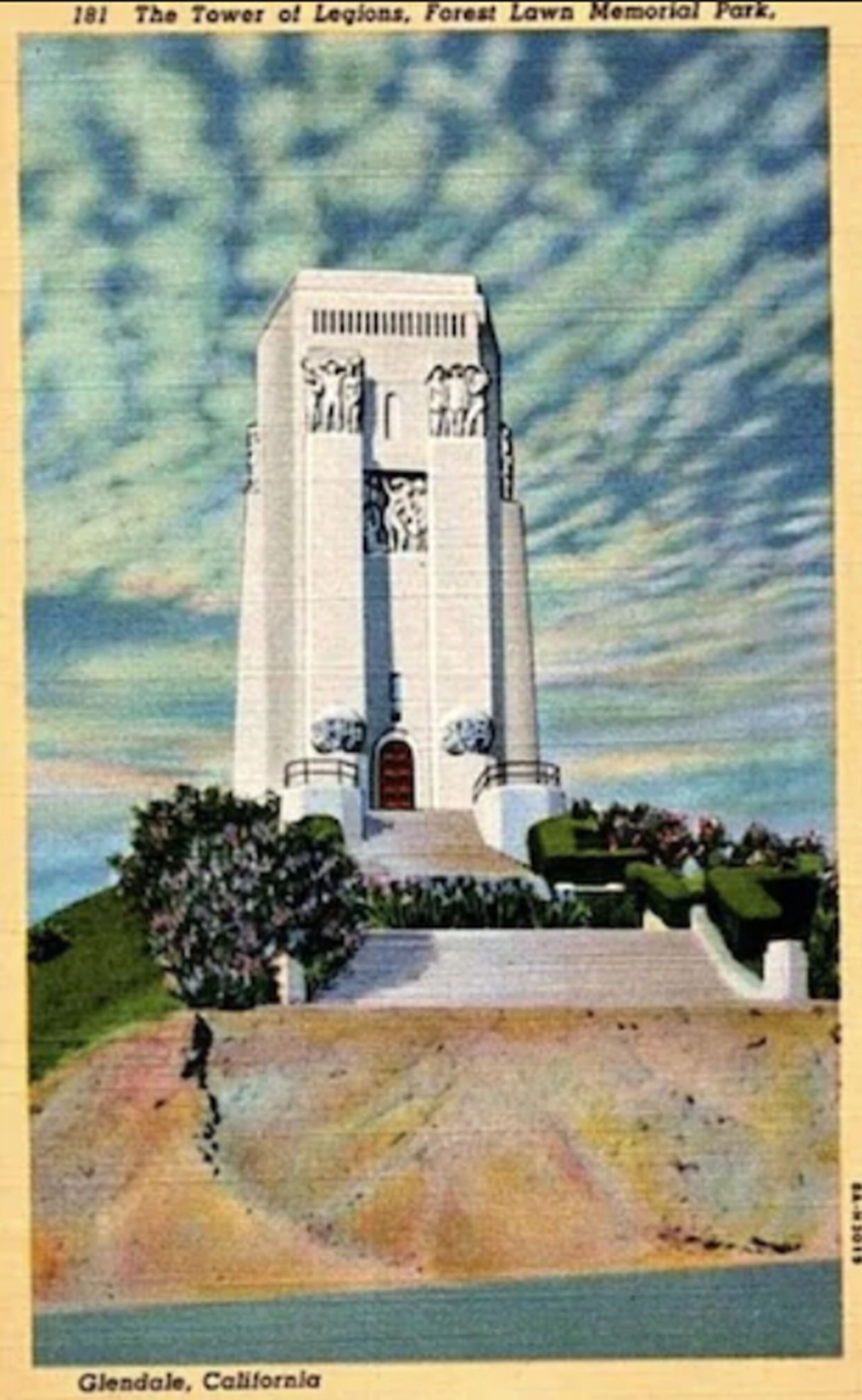 A tall, white tower with statues at the base, located in a park with a clear sky.