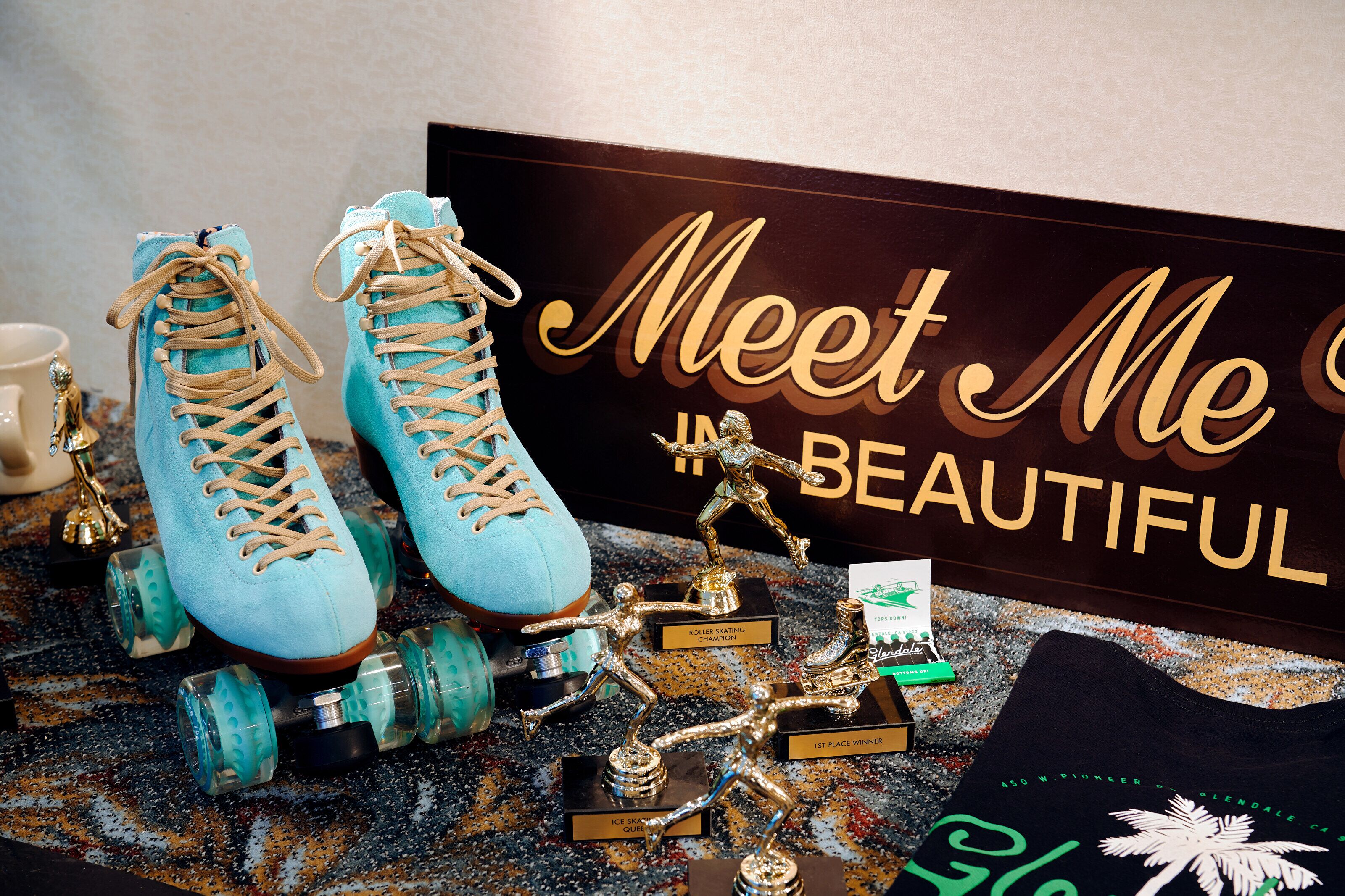 Un par de patines azules claros, un trofeo y un cartel que dice 'Meet Me Beautiful'.