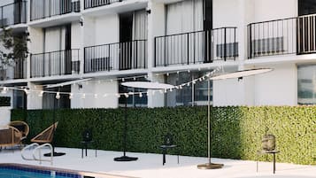 A modern building with multiple balconies, a swimming pool, outdoor seating, and string lights.