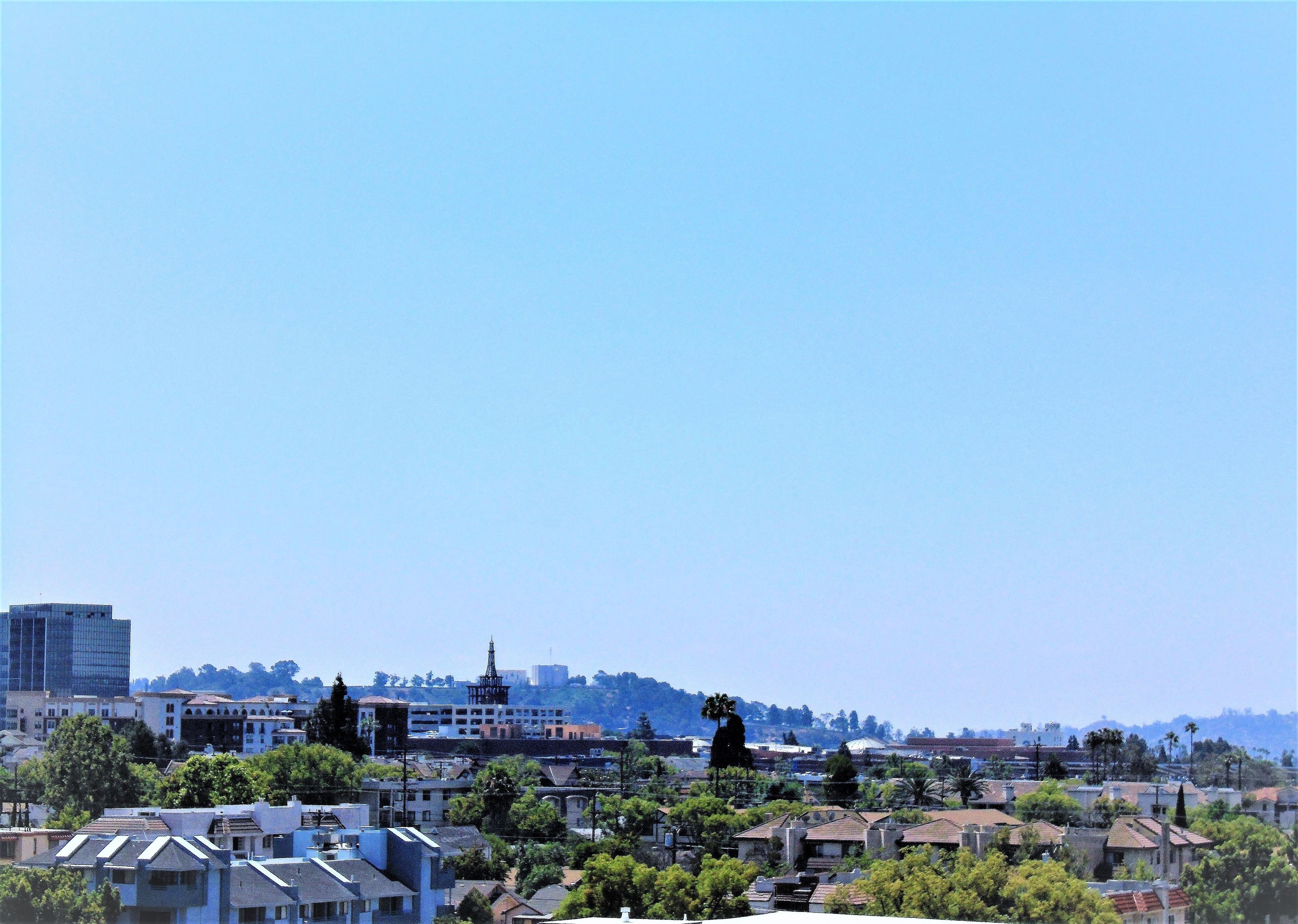 Un paisaje urbano con diversos edificios, incluyendo una edificación blanca destacada con una torre, rodeada de zonas residenciales y vegetación.