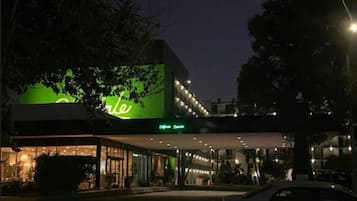 A hotel with a green sign, a covered entrance, and a car parked in front.