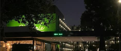 A hotel with a green sign, a covered entrance, and a car parked in front.