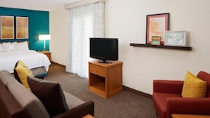 A hotel room with a bed, a TV on a wooden stand, a red sofa, a brown sofa, and a small wooden table.
