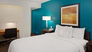 A hotel room with a large bed, a desk, a chair, a lamp, and a painting on the wall.