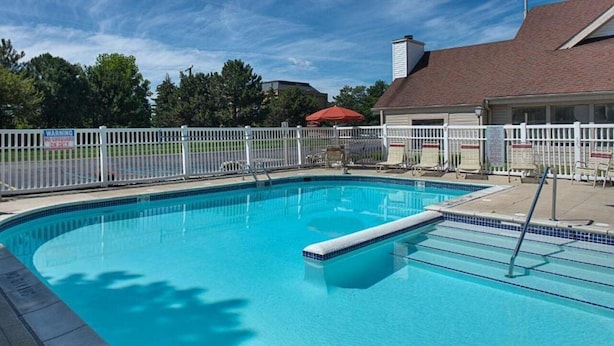A swimming pool with a white fence, lounge chairs, and a building in the background.