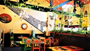 A restaurant with colorful chairs and tables, a staircase with photos on the wall, and hanging plants. - GuestHouse Enumclaw (Enumclaw)